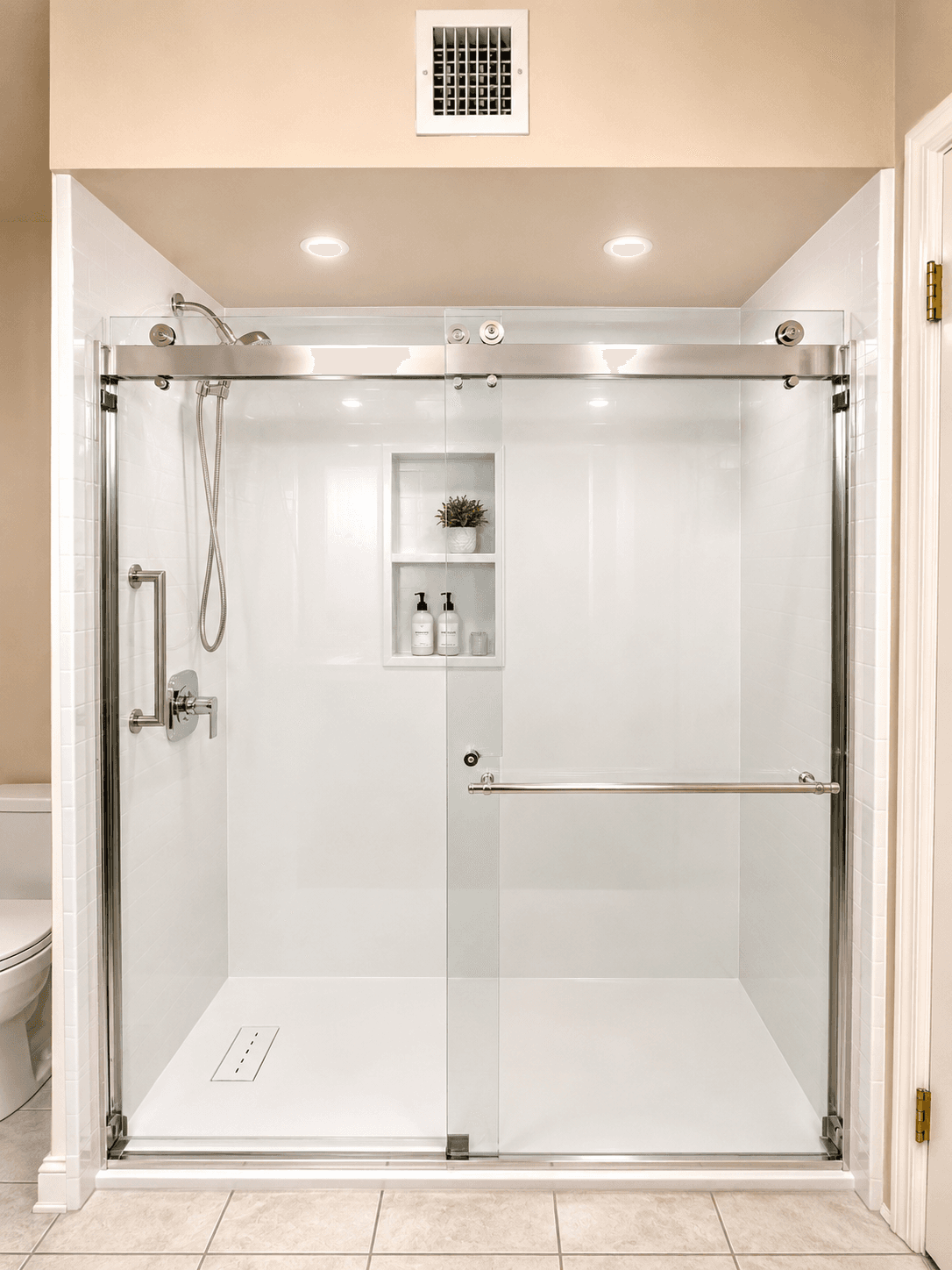 Modern bathroom shower enclosure with sliding glass doors, chrome fixtures, built-in niche with toiletries and plant, and recessed lighting in ceiling